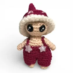Petite figurine champignon Bolet en crochet bordeaux avec salopette et étoiles.