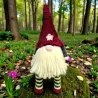 Grand gnome Hector en crochet assis dans la forêt avec bonnet bordeaux et longues jambes rayées.
