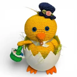 Poussin au crochet jaune avec chapeau haut-de-forme bleu et panier de Pâques dans son œuf sur pieds.